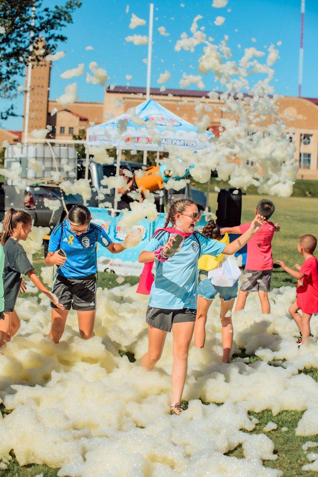 Children play in a field of foam at an LPCA event, laughing and reaching into the bubbles.
